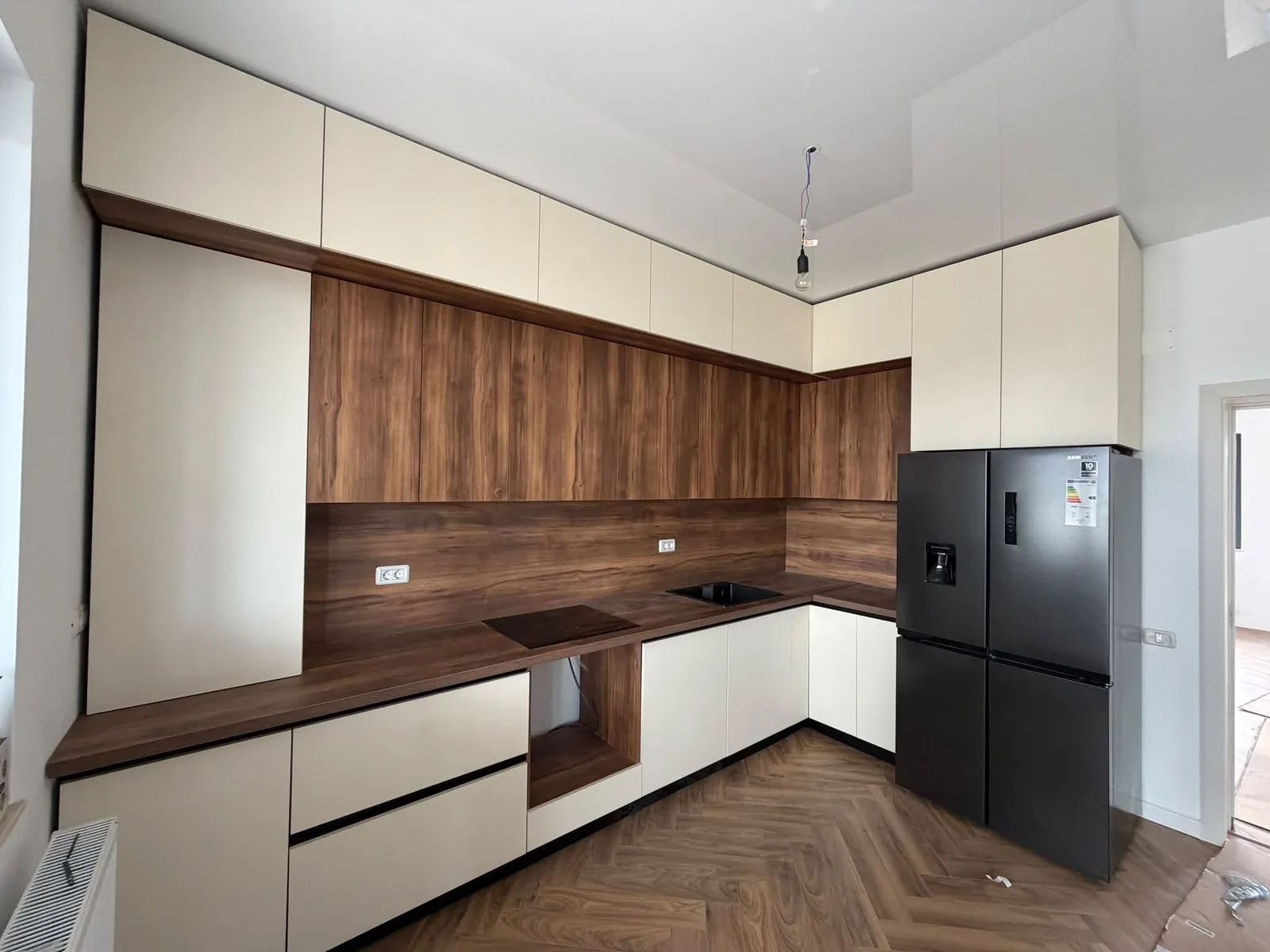 Bucătărie în L cu fronturi crem mat fără mâner, blat și placare în decor nuc
