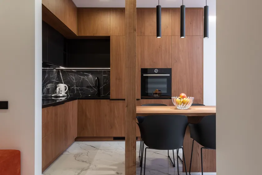 Bucătărie în L cu fronturi decor nuc, corpuri negre și placare imitație marmură